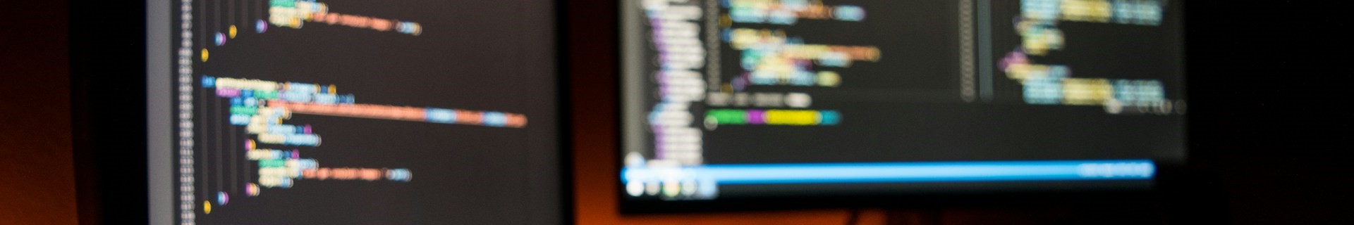 A dual monitor display shows blurry lines of JavaScript and HTML.